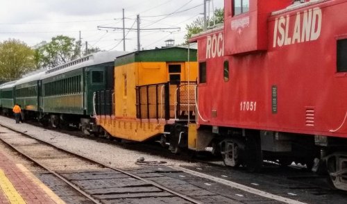 A green and yellow train car next to a red Rock Island caboose at a train station.
