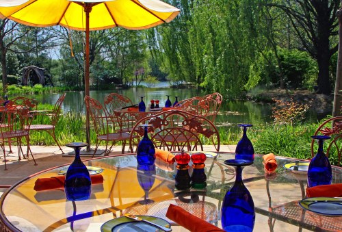 A sunny outdoor dining area by a serene lake, featuring colorful glassware and vibrant orange napkins.