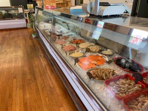 A seafood display case filled with various fresh fish and shellfish on ice in a wooden-floored market.