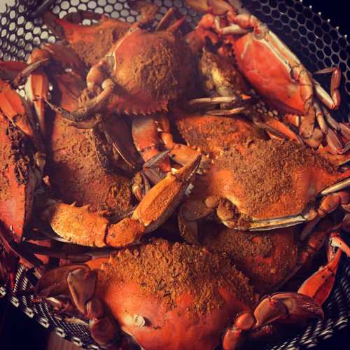 A close-up of a basket filled with seasoned crabs, showcasing their vibrant orange shells and spices.
