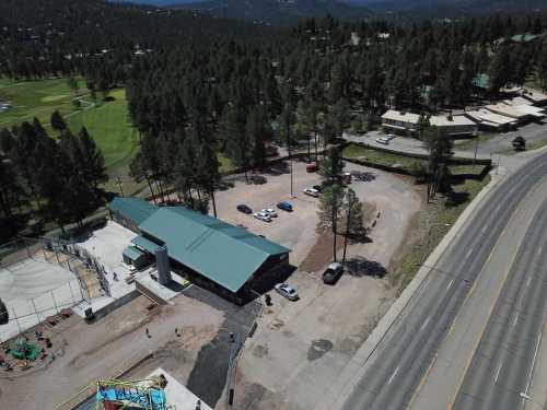 Aerial view of a parking area and building surrounded by trees, with a road and grassy field nearby.