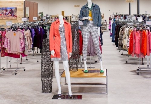 Two mannequins display outfits in a clothing store, surrounded by racks of various apparel.