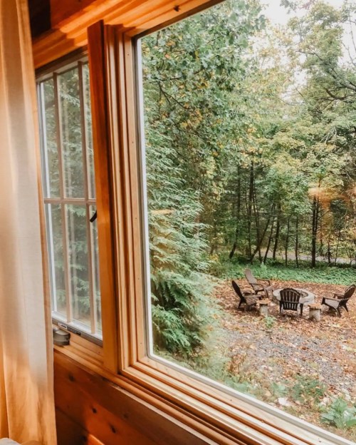 View from a cabin window overlooking a forested area with a circular seating arrangement around a fire pit.