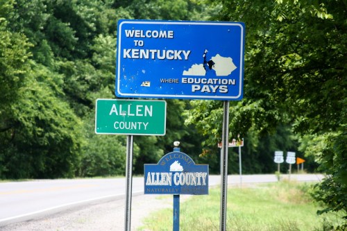 Welcome signs for Kentucky and Allen County, surrounded by greenery along a roadside.