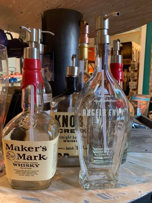 A collection of whiskey bottles, including Maker's Mark and others, displayed on a wooden surface.