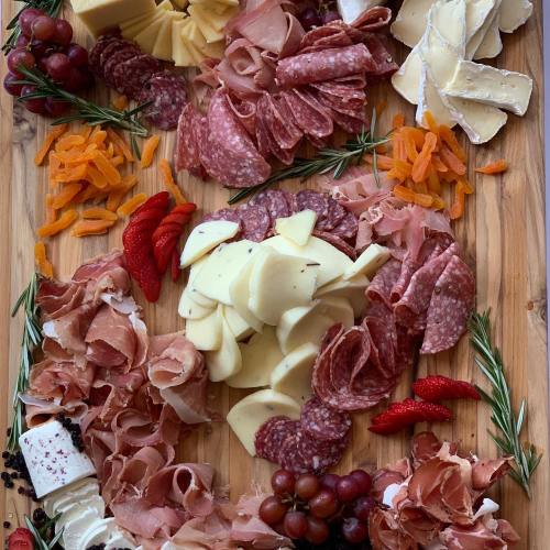 A wooden board arranged with various cheeses, cured meats, fruits, and herbs, creating a colorful charcuterie display.