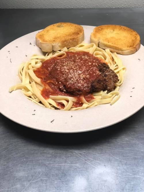 A plate of fettuccine pasta topped with marinara sauce and meat, served with two slices of toasted bread.
