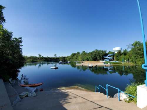 A calm lake surrounded by greenery, with boats on the water and a clear blue sky above.