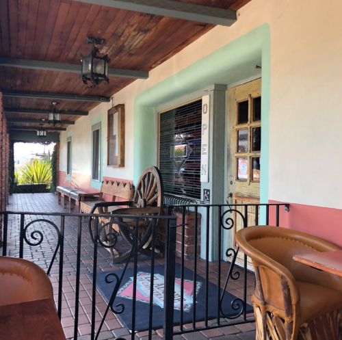 A rustic outdoor seating area with wooden benches, a decorative wagon wheel, and an open door inviting guests inside.