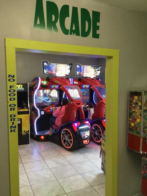 A colorful arcade entrance with a racing game machine and a gumball machine nearby.