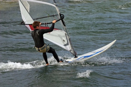 A person windsurfing on a body of water, skillfully maneuvering the sail against the waves.