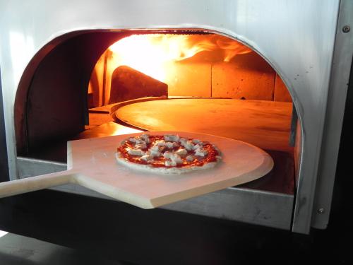 A pizza on a wooden peel, just outside a blazing pizza oven, ready to be cooked.
