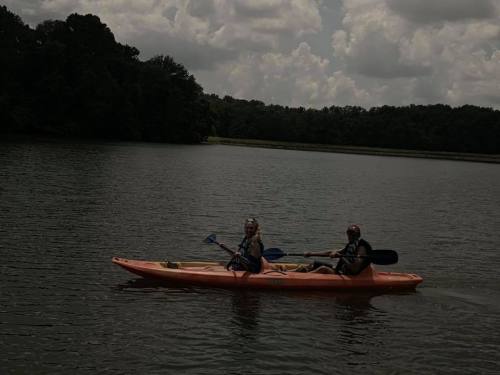 Two people kayaking on a calm lake surrounded by trees under a cloudy sky.