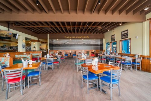 A spacious restaurant interior with wooden floors, colorful chairs, and a large mural on the back wall.