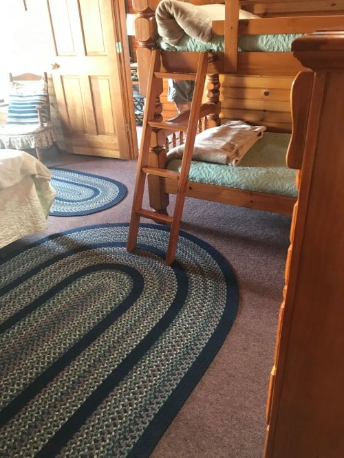 A cozy bedroom featuring a wooden bunk bed, a ladder, and braided rugs on the floor.