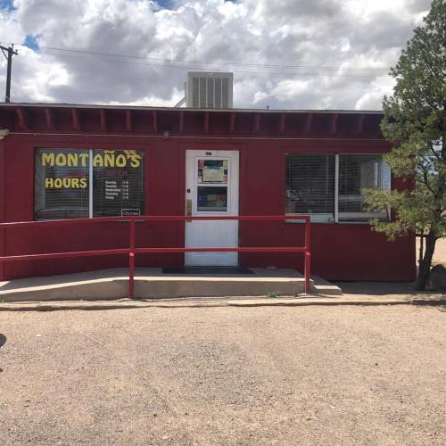 A small red building with a sign reading "Montano's" and visible hours, surrounded by gravel and a few trees.