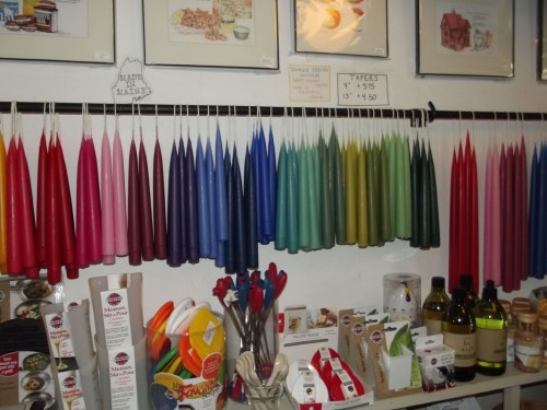 A display of colorful candles hanging on a wall, with various craft supplies and oils on a table below.