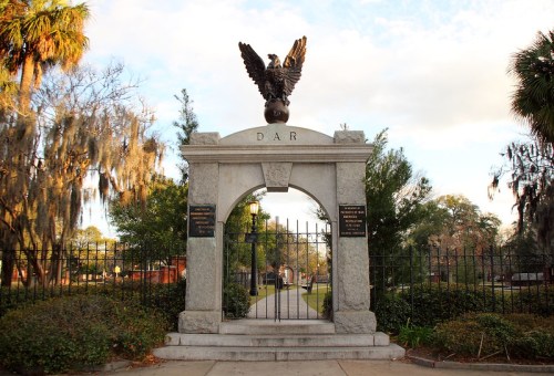 Archway with an eagle sculpture, surrounded by greenery and a pathway, marking a historic site.