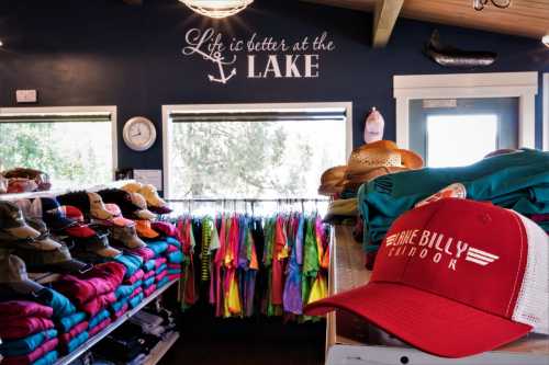 A cozy shop interior with colorful clothing racks and a red cap on display, featuring a "Life is better at the lake" sign.