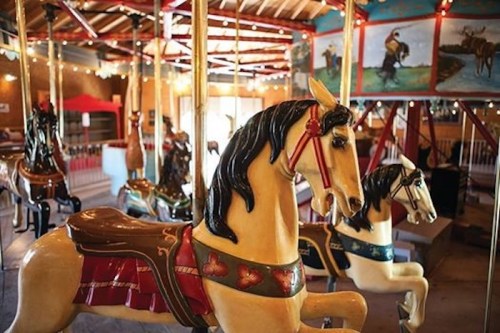 A vintage carousel featuring intricately painted horses in a brightly lit indoor setting.