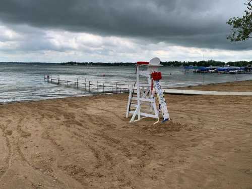 A sandy beach with a lifeguard stand, cloudy skies, and a calm lake in the background.