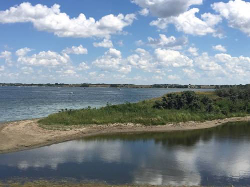 A serene landscape featuring a calm body of water, lush greenery, and fluffy clouds under a bright blue sky.