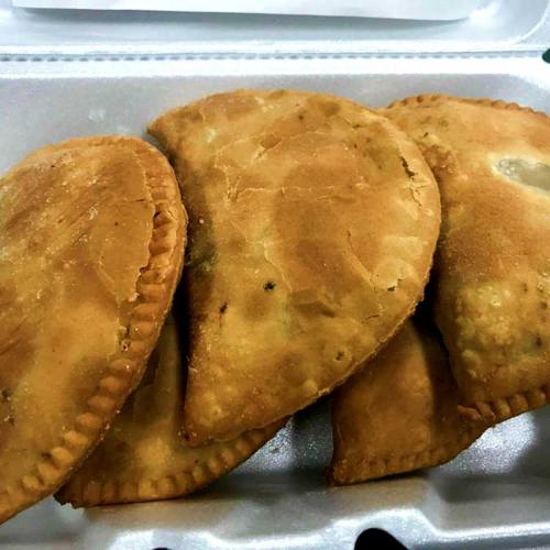 Four golden-brown, fried empanadas arranged in a takeout container.