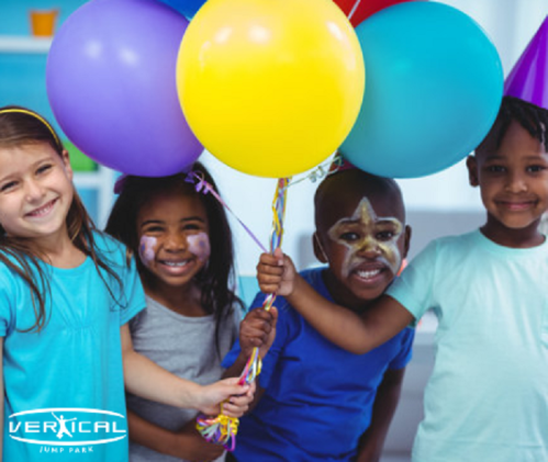 Four children smiling and holding colorful balloons, celebrating a birthday party with face paint and party hats.
