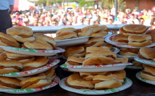 A stack of plates piled high with sandwiches, with a crowd of people blurred in the background.