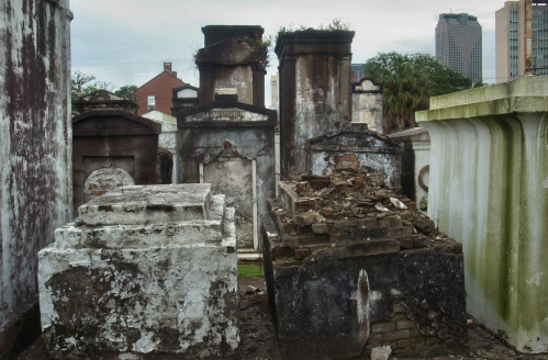A weathered cemetery with old tombs and mausoleums, surrounded by modern buildings in the background.
