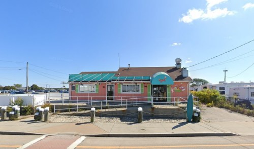 A colorful restaurant with a green awning and pink exterior, surrounded by a parking area and blue sky.