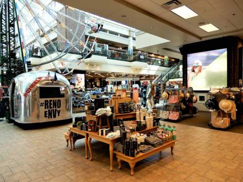 A spacious retail store featuring merchandise displays, an escalator, and a large screen with a promotional image.