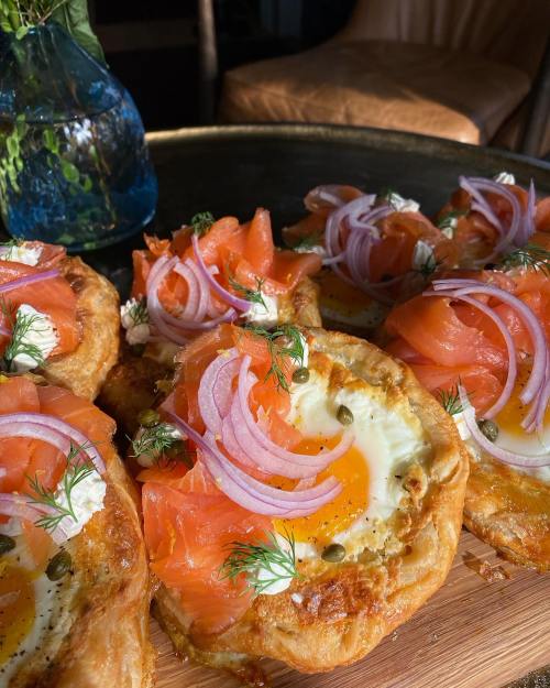 A close-up of pastry topped with smoked salmon, cream cheese, capers, red onion, and fresh dill, served on a wooden platter.