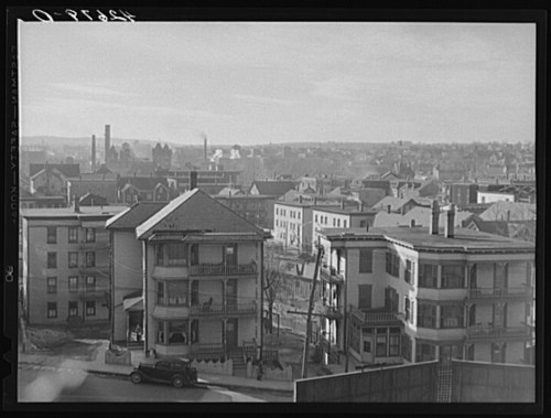 A panoramic view of a cityscape featuring residential buildings and a vintage car parked on the street.