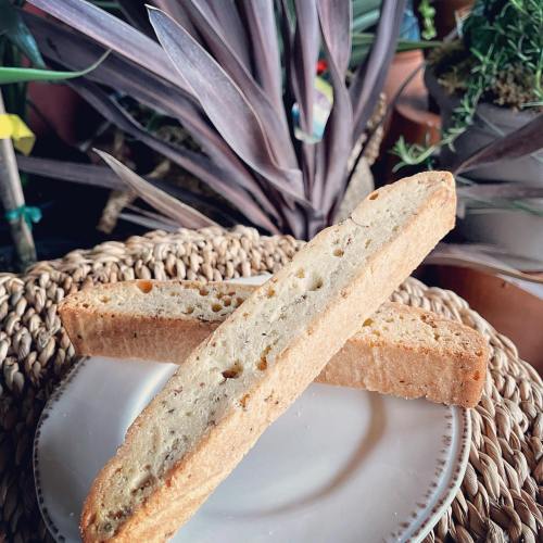 Two pieces of biscotti arranged in a cross on a plate, with plants in the background.