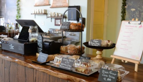 A cozy café counter displaying various baked goods and desserts on glass trays with price tags.