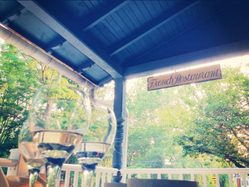 A cozy outdoor dining area with glasses of water and a sign reading "French Restaurant" amidst greenery.
