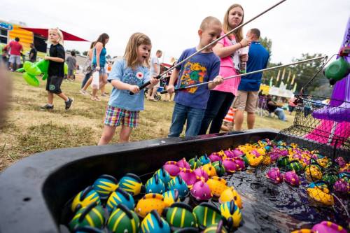 Children playing a carnival game, fishing for colorful toy fish in a water-filled tub at an outdoor fair.