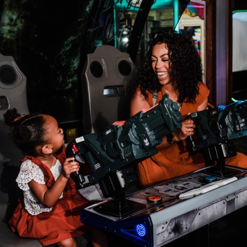 A woman and a young girl joyfully play a video game together, smiling and engaged in the fun.