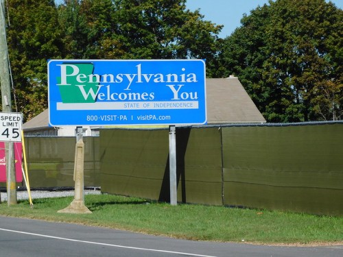 A blue welcome sign for Pennsylvania, stating "Pennsylvania Welcomes You" with a phone number and website below.