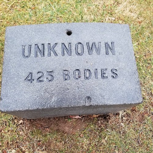 A gray stone marker engraved with "UNKNOWN. 425 BODIES" on a grassy area.