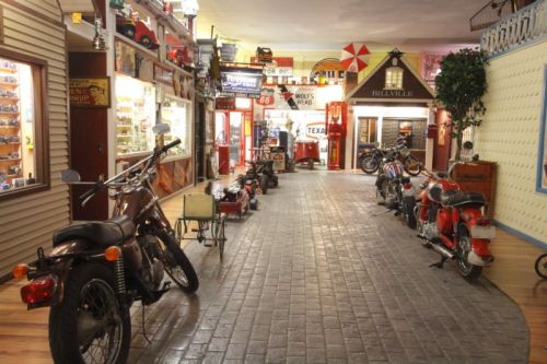A vintage-themed indoor space featuring classic motorcycles, retro signs, and nostalgic decor along a brick pathway.