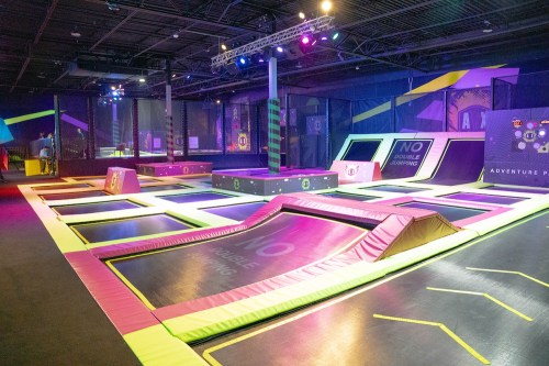 A vibrant indoor trampoline park featuring multiple trampolines, foam pits, and colorful lighting.