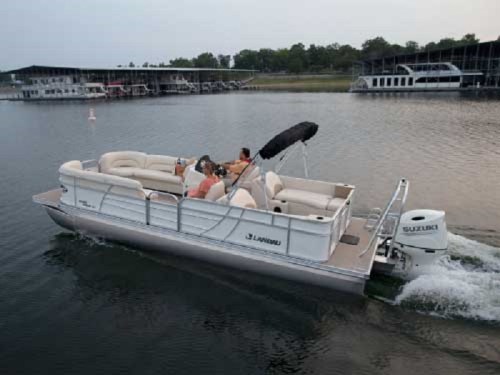 A pontoon boat with passengers cruising on calm water near a marina at sunset.