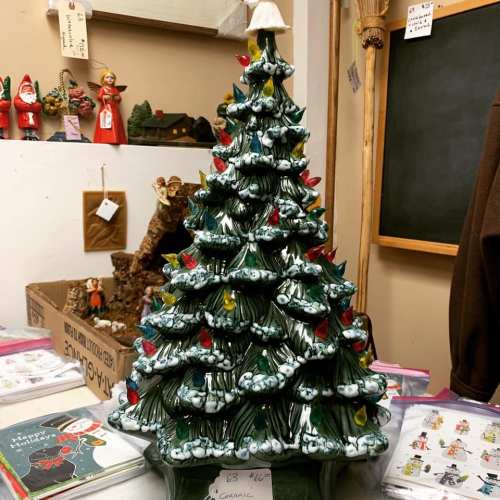 A ceramic Christmas tree with colorful lights, displayed in a cozy shop filled with holiday decorations.