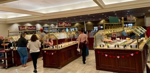 A busy buffet restaurant with customers serving food from various stations and a warm, inviting atmosphere.