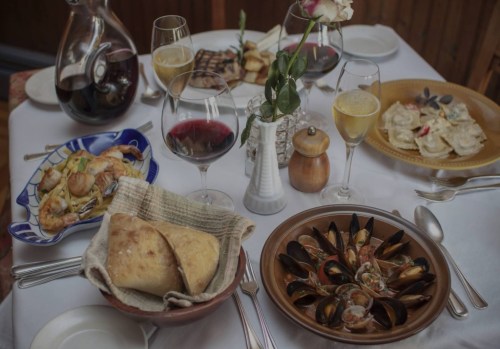 A beautifully set table with various dishes, including seafood, pasta, bread, and drinks, surrounded by elegant tableware.