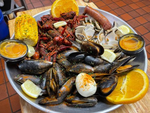 A seafood platter featuring crawfish, clams, mussels, sausage, corn, and garnished with lemon and orange slices.