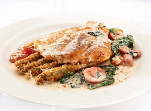 A plated dish featuring breaded chicken, creamy sauce, spinach, tomatoes, and crispy green beans on a white background.