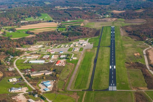 Aerial view of a rural airport with a runway, surrounded by fields and small buildings.
